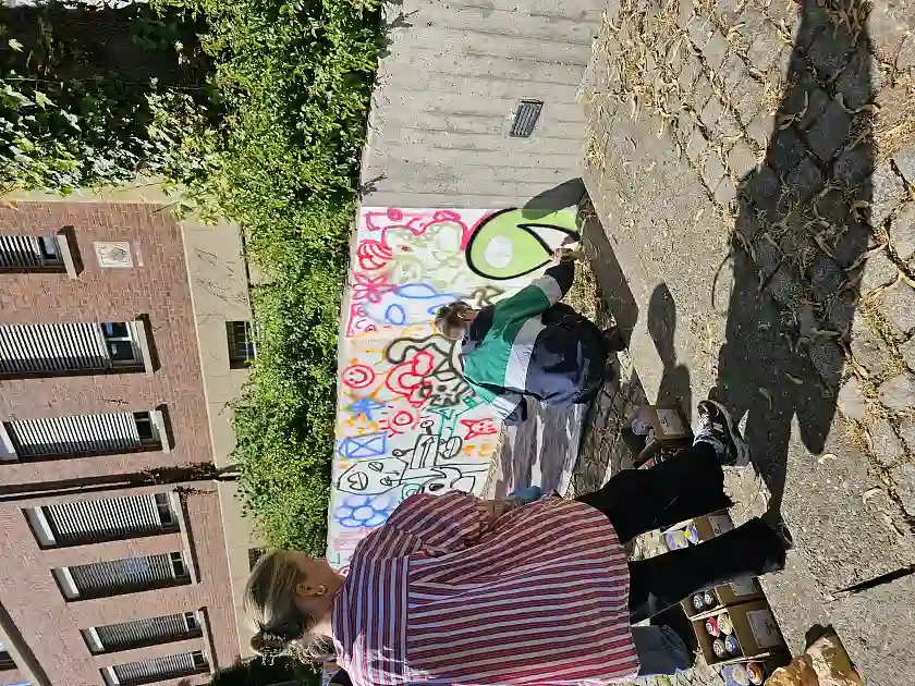 Zusehen ist der K&uuml;nstler, der den Sch&uuml;ler:innen eine Technik zum Ausmalen zeigt